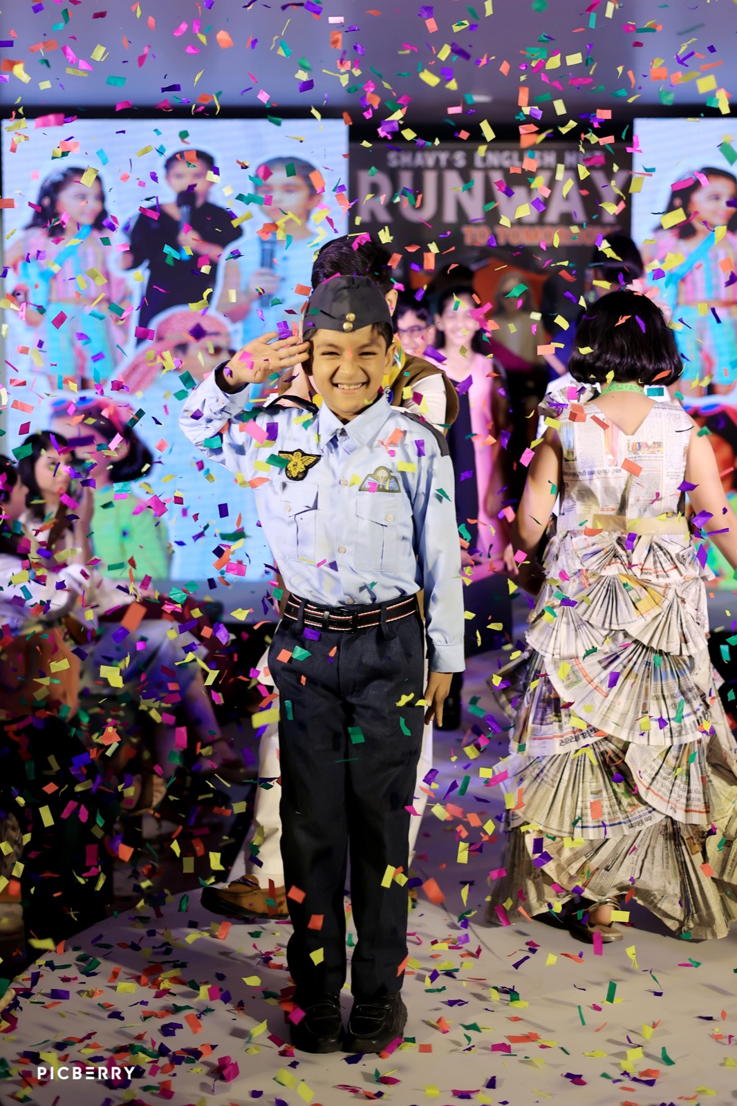 Student in a pilot costume saluting amid confetti at the Runway to Tomorrow fashion show